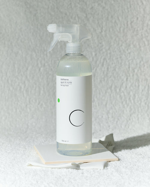 Spruteflaske med multispray i duften agurk og mynte foran hvitt håndkle.
